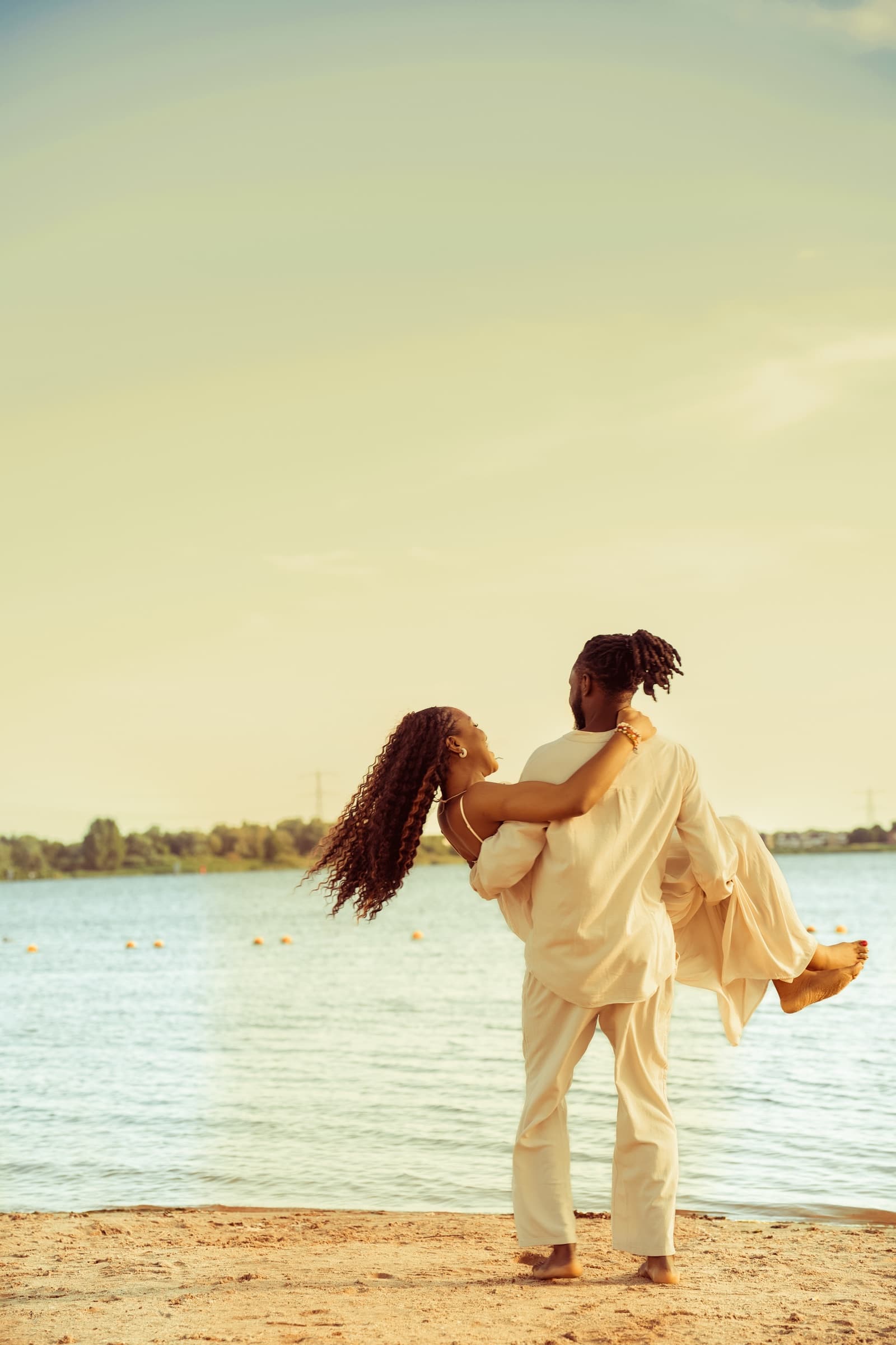 Couple at the water's edge at golden hour, one carrying the other