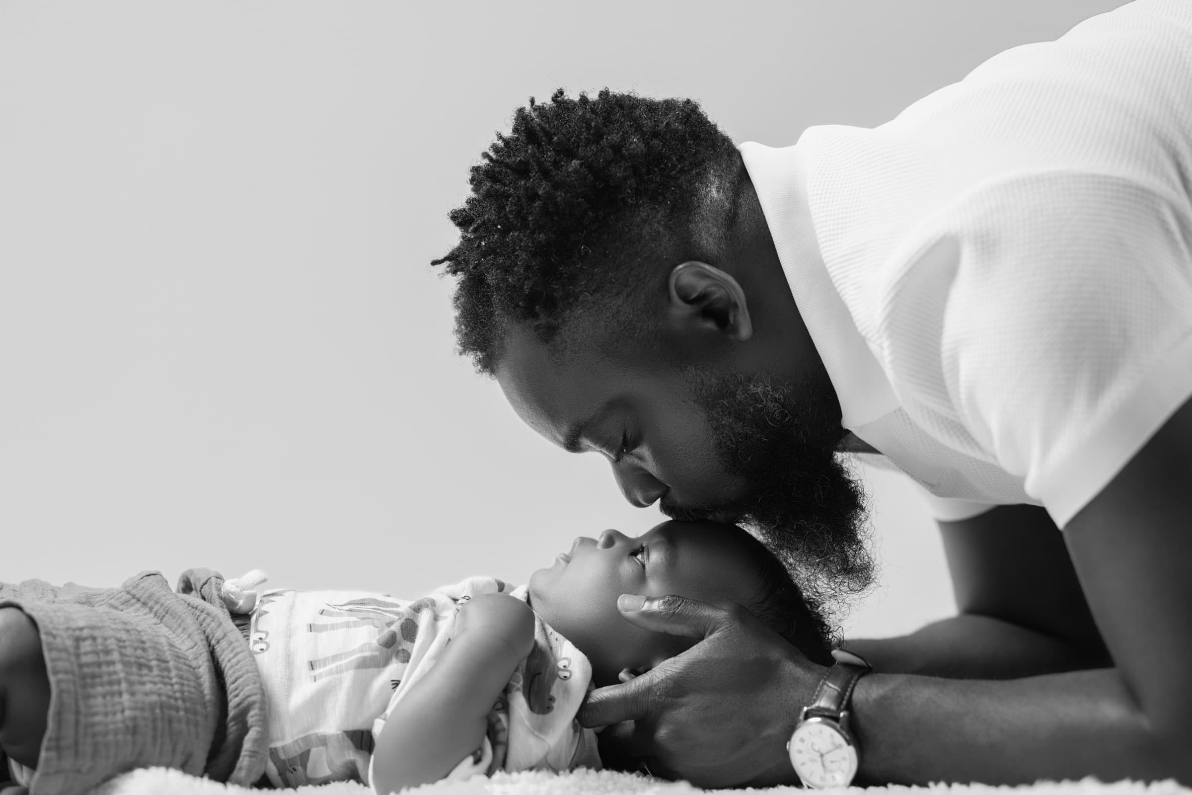 Black and white portrait of a father kissing his baby's forehead