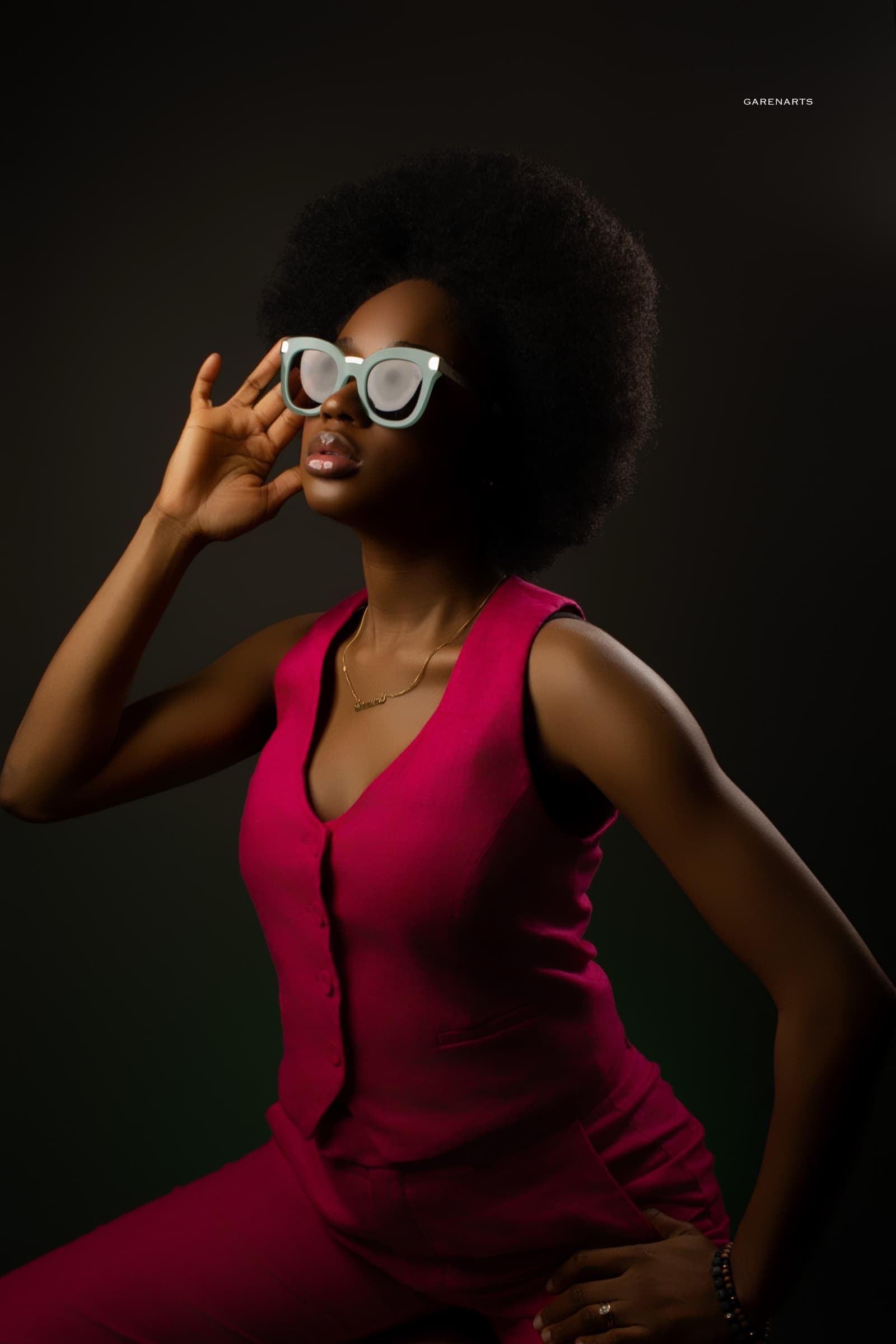 Editorial studio portrait of a woman in a magenta suit and white sunglasses